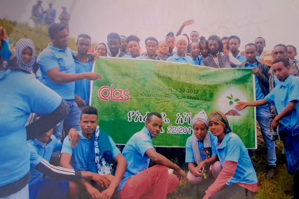 Colas staff in blue shirts holding a green Green Legacy banner printed with the Colas logo and the date Adoleessa 22, 2011.